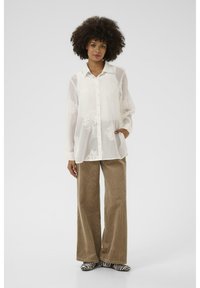 White sheer blouse with floral embroidery, paired with light brown wide-leg corduroy pants and black-and-white striped shoes.