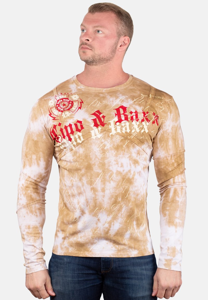 Het shirt met lange mouwen heeft een bruin en wit tie-dye patroon, met rode tekst en logo graphics. Gemaakt van katoen, heeft het een getailleerde snit.
