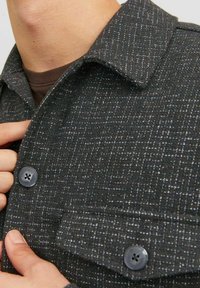 Camicia button-up scura con una trama testurizzata e un motivo sottile, colletto a punta e taschino con chiusura a bottone rotondo.