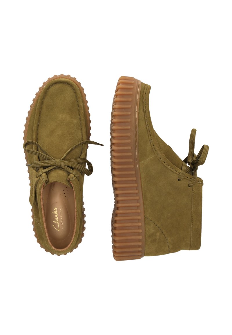 Zapatos de ante verde oliva con suela de goma gruesa y texturizada. Presentan un diseño con cordones, puntera redondeada y detalles de costura visibles.
