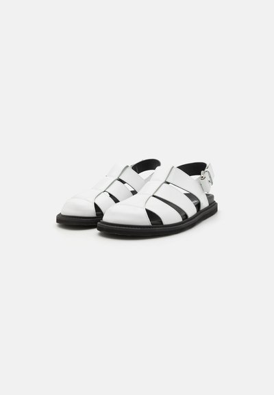 White leather sandals with black accents. Features open design, multiple wide straps, and a back strap with adjustable buckle. Flat sole.
