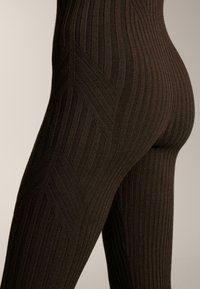 Približni prikaz nogu u tamnocrnim rebrastim pletenim tajicama s cik-cak uzorkom na bedrima na neutralnoj pozadini.