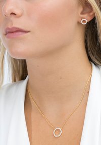 Guldhalsband och matchande örhängen har cirkulära mönster med klara stenar. Halsbandet har en delikat kedja och en framträdande ädelstensaccent.