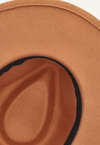 Bruine vilten hoed met brede rand, met een gladde textuur en een zwarte accentband langs de binnenrand. Zachte, afgeronde vorm en gelijkmatige kleur.