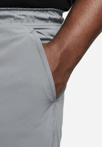 Main à la peau foncée partiellement dans la poche avant d'un pantalon gris clair à taille élastique.