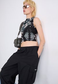 Svart tie-dye crop top med høy hals, parret med svarte cargo bukser med sidelommer og en hvit Nike-logo. Tilbehør inkluderer solbriller og en liten skulderveske.