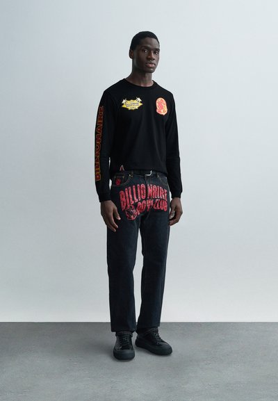 Μαύρο μακρυμάνικο πουκάμισο με πολύχρωμα σχέδια στο μπροστινό μέρος και στο μανίκι. Σκούρο τζιν με έντονο κόκκινο κείμενο και γραφικά στο πίσω μέρος. Μαύρα παπούτσια.