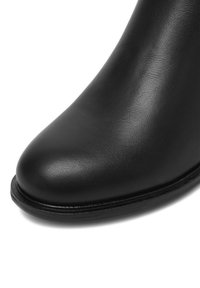 Čierna kožená členková topánka s okrúhlym špičkou, hladkou textúrou a pevným podošvou. Jemné prešívanie pozdĺž okrajov.