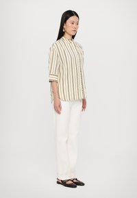 Striped lightweight blouse with a high collar, half sleeves, and button closure, paired with white trousers and dark flat shoes.
