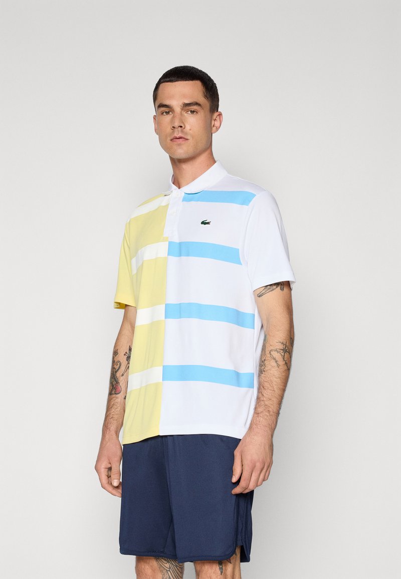 Polo à manches courtes avec des rayures horizontales jaunes, blanches et bleues, présentant un col classique et un logo vert sur la poitrine.