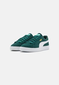 Sneaker in camoscio verde con suole in gomma bianca, caratterizzate da un design a strisce e da una marchiatura dorata sul lato. I lacci sono dello stesso colore delle scarpe.
