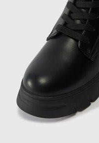 Μαύρη δερμάτινη μπότα μέχρι τον αστράγαλο με στρογγυλή μύτη, υφασμάτινη επιφάνεια, χοντρή καουτσούκ σόλα και μαύρους κορδόνες. Διαθέτει μινιμαλιστικό σχέδιο.