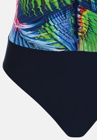Badedragt i ét stykke med et livligt tropisk print i grøn, blå og pink øverst, kontrasteret af en ensfarvet marineblå bund. Glat tekstur.