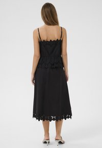 Black mid-length dress with layered ruffled design, scalloped edges, and eyelet details. Spaghetti straps and smooth fabric texture.