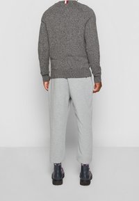 Grauer Strickpullover mit strukturiertem Finish, kombiniert mit hellgrauen Jogginghosen. Die Schuhe haben ein knöchelhohes Design in dunkler Farbe und sind mit gemusterten Socken kombiniert.