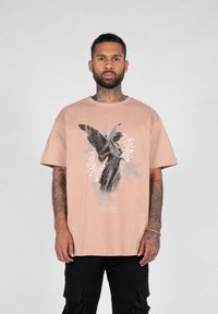 Light pink short-sleeve t-shirt featuring a graphic of a winged statue, with gray accents and text at the bottom. Casual fit, soft texture.