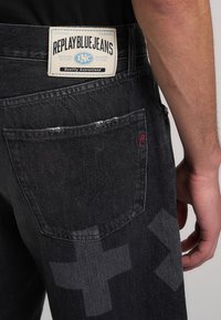 Jeans in denim nero con etichetta del marchio sulla cintura posteriore, due tasche posteriori con accenti rossi e sottili motivi geometrici.