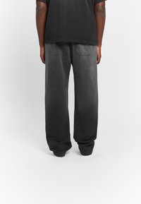 Dark gray, loose-fitting pants with a textured finish. Features a back pocket, wide legs, and subtle color gradient towards the bottom.