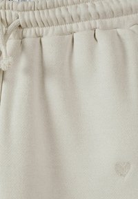 Beige fleecebyxor med elastisk midjeband och dragsko, strukturerat tyg och en liten broderad hjärtdetalj.