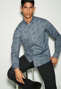Camicia button-up in navy con motivo paisley. Presenta un colletto classico, maniche lunghe e una vestibilità slim. Indossata con pantaloni neri.