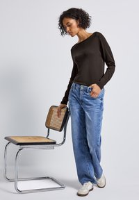 Donker lange mouwen top gedragen met lichtblauwe wijdvallende jeans, met zakken en een losse pasvorm. Stoel met een matzwart frame en een rotan zitting.