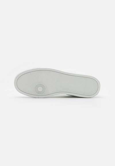 Fehér sneaker talp sima felülettel, kör alakú logó részlettel és diszkrét, texturált tapadási mintával. A szélén enyhén kiemelkedik.