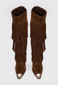 Botas de ante marrón hasta la rodilla con flecos en capas y punteras metálicas en forma de punta. Textura suave con una silueta delicada.