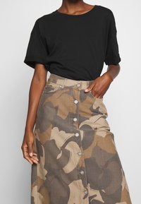 Black short-sleeve t-shirt paired with a knee-length, patterned skirt featuring large, abstract camouflage shapes in tan and gray tones, with button detail.
