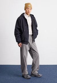 Navy niebieska kurtka z kapturem na lekką koszulę, szare spodnie z kordurowej tkaniny i szare trampki. Czapka beanie jest w kolorze tan z naszywką logo. Gładkie tekstury, swobodny krój.