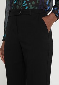 Černé upravené kalhoty se slim fit, vybavené bočními kapsami a jedním zapínáním na knoflík, vyrobené z hladkého, texturovaného materiálu.