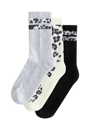 Three pairs of ribbed crew socks in gray, white with black leopard spots, and solid black with a patterned band near the top.