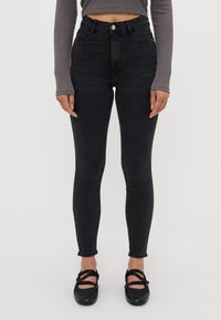 Črne skinny jeans hlače z visokim pasom, z zapiranjem na sprednji gumb in subtilnim zbledelem izgledom. V kompletu s črnimi sandali na trak.