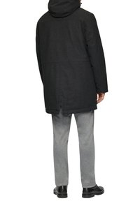 Manteau à capuche noir avec une coupe droite, en tissu mélange de laine, associé à un pantalon de jogging gris et des chaussures noires.
