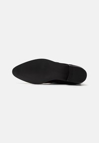 Suela de zapatos de cuero negro con un acabado suave y un diseño de punta afilada. Presenta sutiles estrías para mayor tracción en la parte inferior.