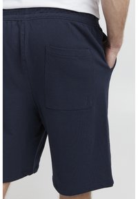 Pantaloni corti in cotone blu navy con cintura elastica, dotati di una tasca posteriore e di una vestibilità comoda. Il tessuto ha una texture liscia e una leggera elasticità.