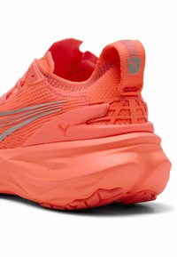 Chaussure de course Puma en corail vif, dotée d'un upper en tricot texturé, d'accents en argent réfléchissant et d'une semelle épaisse et rembourrée avec un motif de semelle.