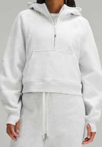 Sweat à capuche court gris clair en tissu doux, avec poche avant, fermeture à demi-zip et ourlet à cordon de serrage. Finition texturée sur les manches.
