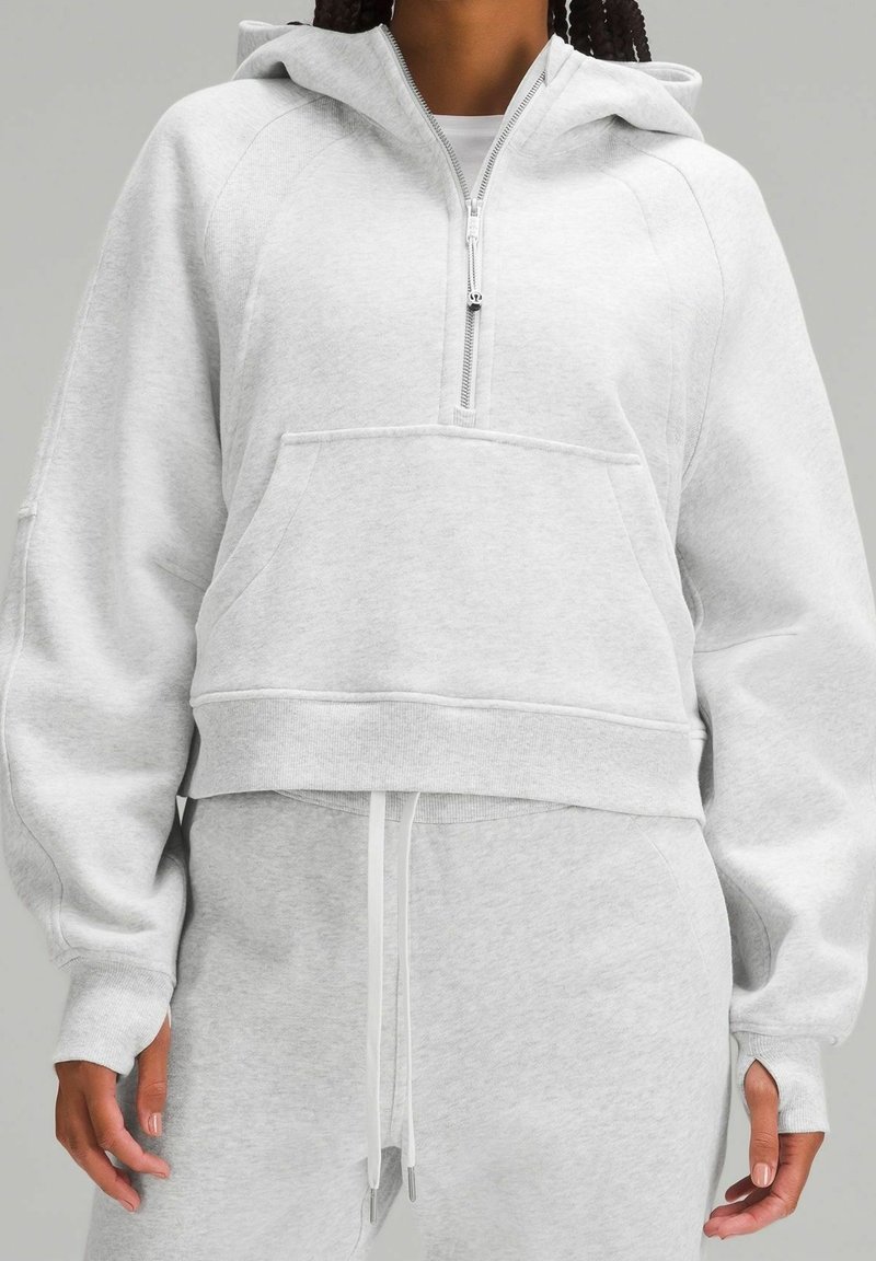 Sweat à capuche court gris clair en tissu doux, avec poche avant, fermeture à demi-zip et ourlet à cordon de serrage. Finition texturée sur les manches.