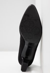 Semelle de chaussure habillée noire pointue montrant des pièces embossées, le marquage "KAISER" et la taille 43 ½ par Peter Kaiser sur fond blanc.