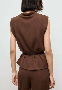 Top tricotat maro fără mâneci cu un design peplum; prezintă un curea din piele închisă la talie și o textură netedă.