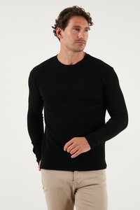 Maglietta nera a maniche lunghe in tessuto a costine con scollatura rotonda, tessuto testurizzato, forma aderente e cuciture sottili, abbinata a pantaloni chiari.