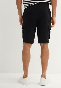 Shorts cargo neri in tessuto texturizzato, con due tasche laterali e cintura elastica, abbinati a sneaker bianche.