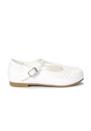 Białe buciki typu Mary Jane z materiałową cholewką, wyposażone w pasek z srebrną klamrą, teksturowane ozdoby oraz płaską gumową podeszwę.