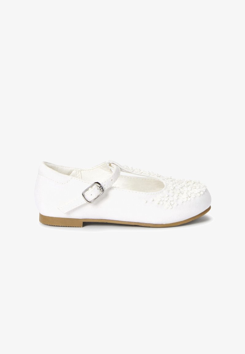 Chaussures Mary Jane blanches avec une tige en tissu, dotées d'une bride avec boucle argentée, d'ornements texturés et d'une semelle en caoutchouc plate.