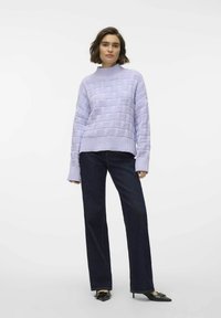 Ljuslila stickad tröja med en strukturerad mönster, hög halsringning och vida ärmar, tillsammans med mörka jeans med rak passform.