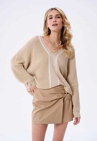 Beige oversized knit sweater with white stripe detail paired with a fitted beige faux leather skirt featuring a side button.