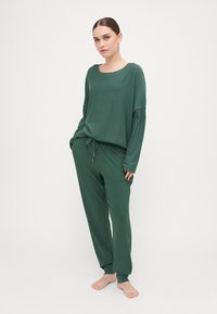 Green two-piece lounge set made of soft fabric. Long-sleeved top with a loose fit and drawstring waist pants; minimal design, no visible patterns.