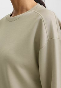 Lys olivengrøn sweatshirt med rund halsudskæring, blød tekstur og let afslappet pasform. Har raglanærmer og minimal syning.