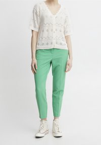 Person wearing a white short-sleeve knit button-up top, mint green slim-fit pants, and high-top white sneakers against a plain background.