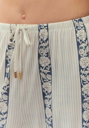 Mittelteil mit beiger Haut und weißer Hose mit vertikalen blauen Blumenmustern und einem zugeschnürten Kordelzug mit goldenen Enden.